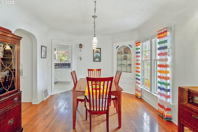 dining space with hardwood / wood-style floors, arched walkways, a textured ceiling, and visible vents