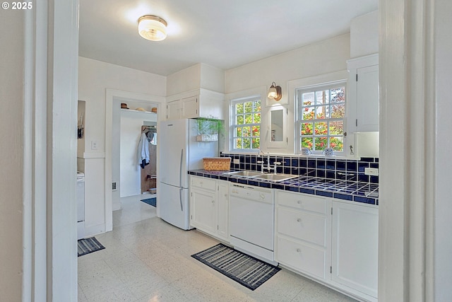 kitchen with a sink, white cabinets, light floors, tile counters, and white appliances