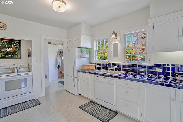kitchen with white cabinets, a sink, white appliances, tile countertops, and light floors