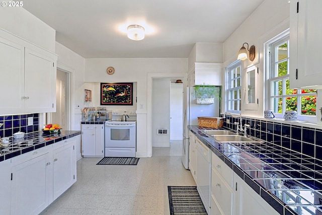 kitchen with a sink, white appliances, tile counters, white cabinetry, and light floors