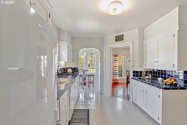 kitchen with decorative backsplash, fridge, light floors, white cabinets, and arched walkways
