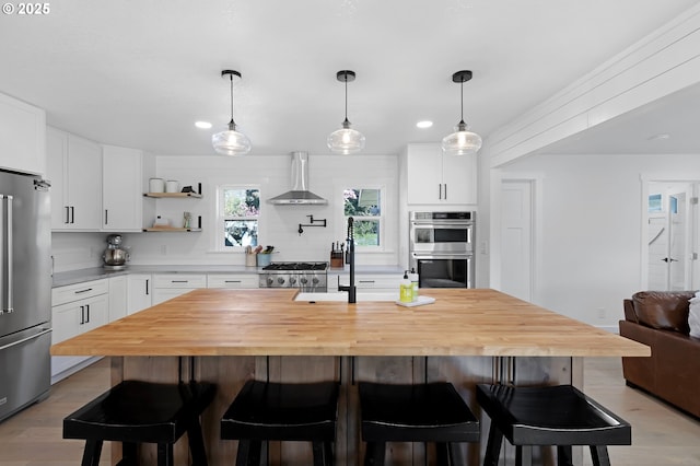 1069 Little Valley Rd, Roseburg, OR 97471 - kitchen featuring appliances with stainless steel finishes, wall chimney exhaust hood, white cabinetry, recessed lighting, and a kitchen bar