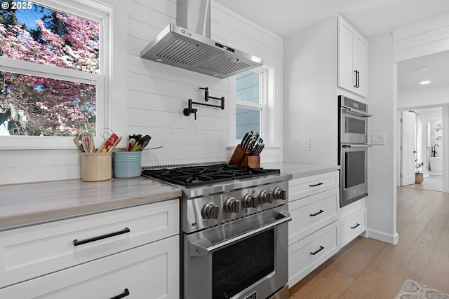 1069 Little Valley Rd, Roseburg, OR 97471 - kitchen featuring appliances with stainless steel finishes, wall chimney exhaust hood, white cabinetry, light wood finished floors, and light stone countertops