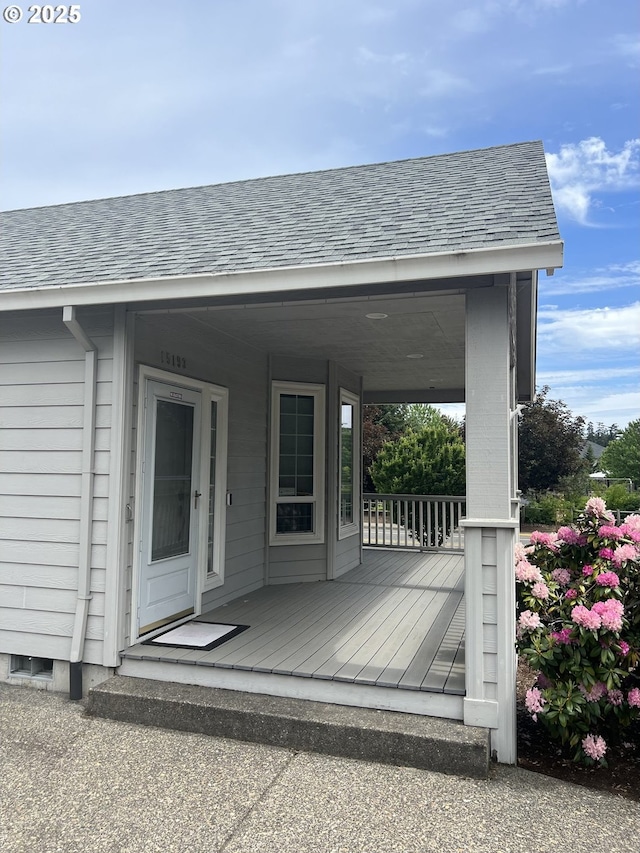 doorway to property featuring a porch and a shingled roof