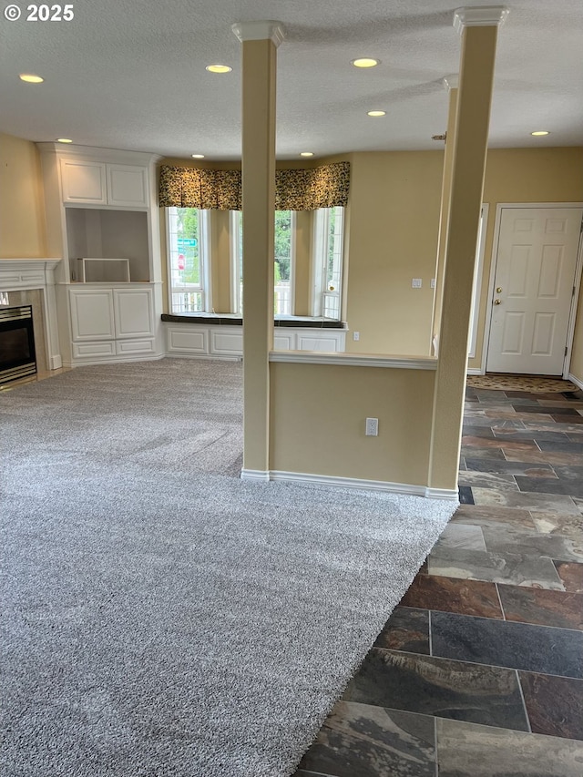 unfurnished living room featuring stone finish floors, recessed lighting, ornate columns, baseboards, and a textured ceiling