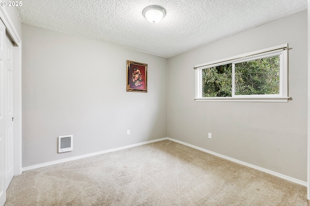 carpeted empty room with visible vents, baseboards, and a textured ceiling