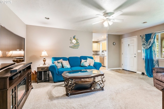 living area featuring light carpet, baseboards, a textured ceiling, and ceiling fan