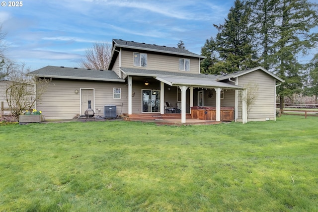 rear view of property featuring central AC unit, fence, a lawn, and a hot tub