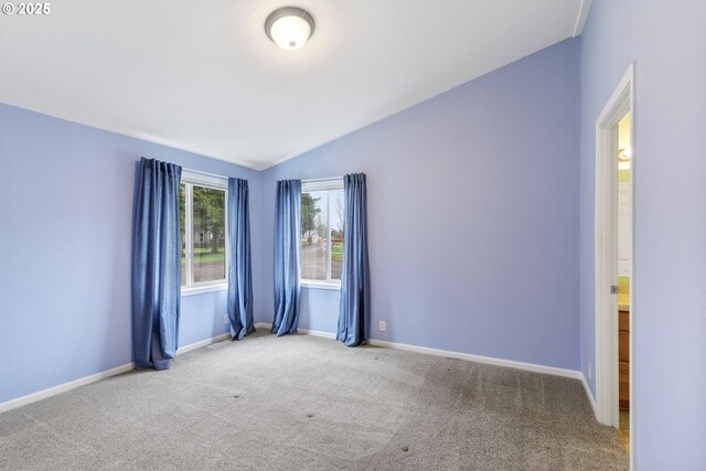 carpeted empty room featuring vaulted ceiling and baseboards