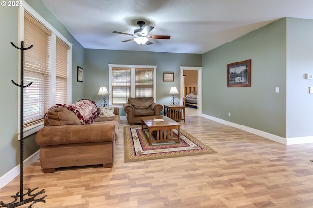 living room with ceiling fan, a textured ceiling, baseboards, and wood finished floors