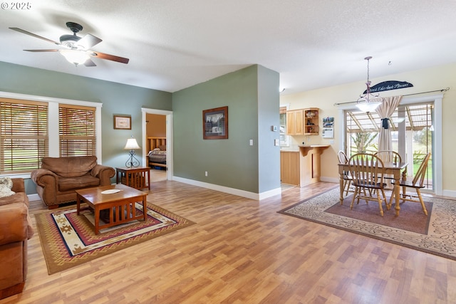 living room featuring ceiling fan, baseboards, a textured ceiling, and wood finished floors