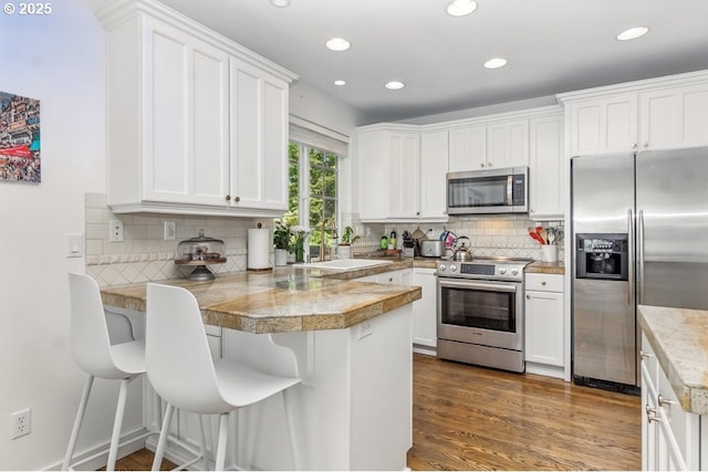 10272 NW Edgewood Dr, Portland, OR 97229 - kitchen with stainless steel appliances, a peninsula, a sink, white cabinets, and recessed lighting