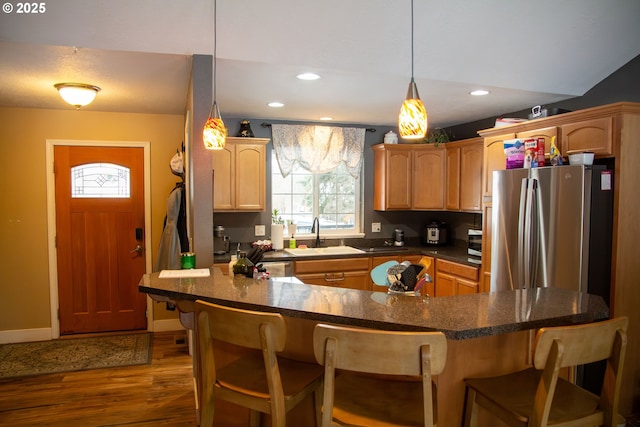 kitchen featuring sink, hanging light fixtures, stainless steel refrigerator, a kitchen breakfast bar, and dark hardwood / wood-style flooring