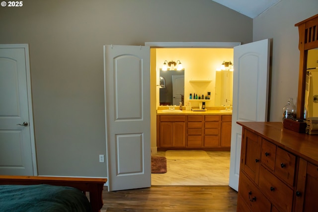 bedroom with lofted ceiling, sink, ensuite bathroom, and light wood-type flooring