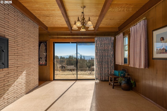 unfurnished room with wooden walls, a chandelier, wooden ceiling, beamed ceiling, and a mountain view