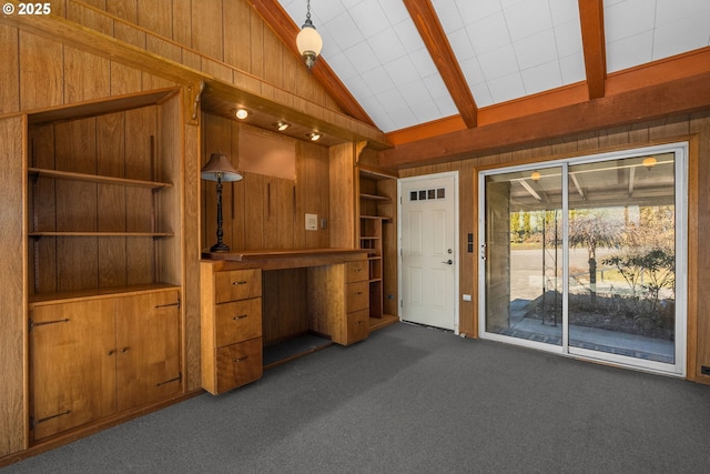 interior space with built in features, built in study area, lofted ceiling with beams, wood walls, and dark carpet