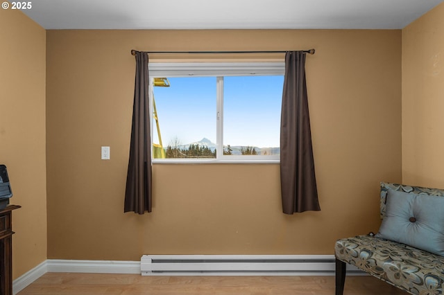 sitting room featuring baseboards, a baseboard heating unit, and wood finished floors