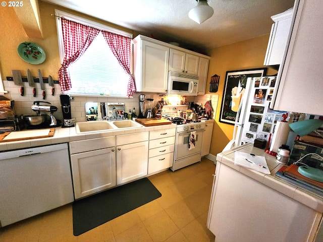 kitchen with sink, tile counters, white cabinets, and white appliances