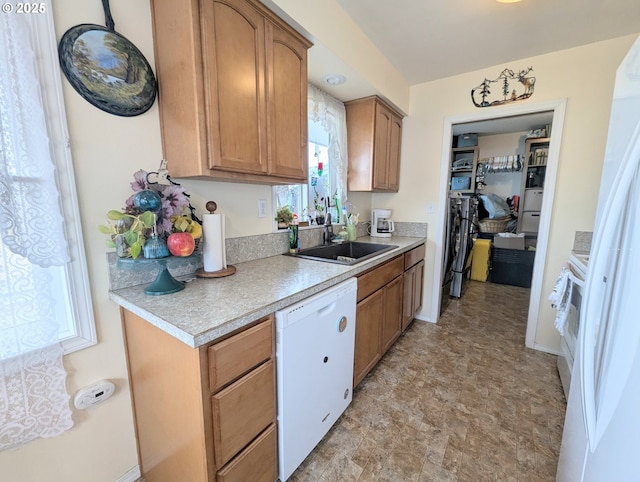 kitchen with light countertops, brown cabinetry, white dishwasher, and a sink