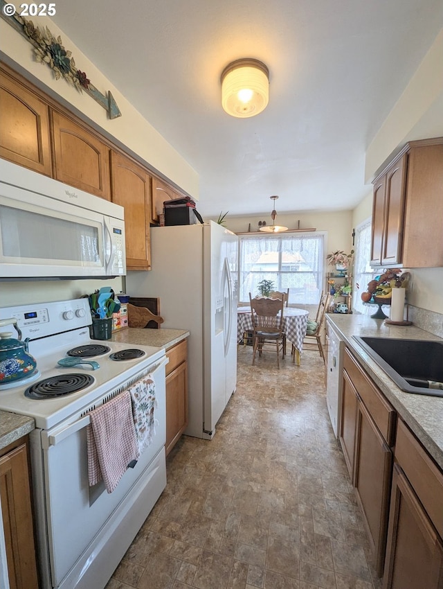 kitchen with brown cabinets, a sink, stone finish flooring, white appliances, and light countertops