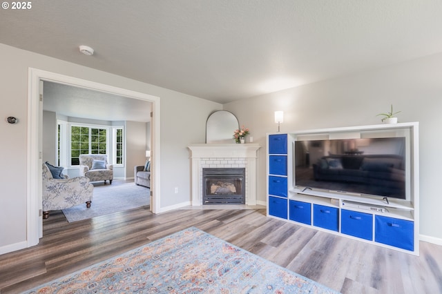 living area with baseboards, a brick fireplace, and wood finished floors
