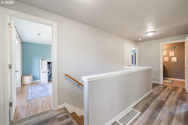 corridor with baseboards, an upstairs landing, wood finished floors, and visible vents