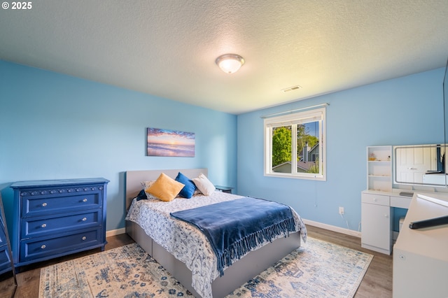 bedroom with baseboards, a textured ceiling, wood finished floors, and visible vents