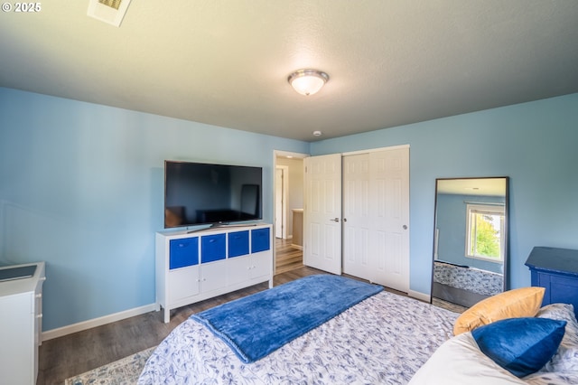 bedroom featuring baseboards, a closet, wood finished floors, and visible vents