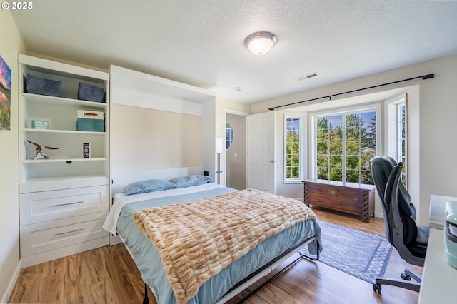 bedroom with baseboards, a textured ceiling, visible vents, and wood finished floors