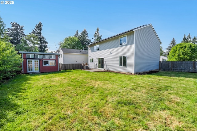 rear view of house featuring a fenced backyard, an outbuilding, a lawn, and french doors