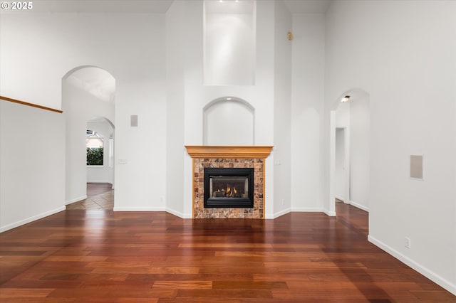 unfurnished living room featuring dark hardwood / wood-style flooring, a stone fireplace, and a high ceiling