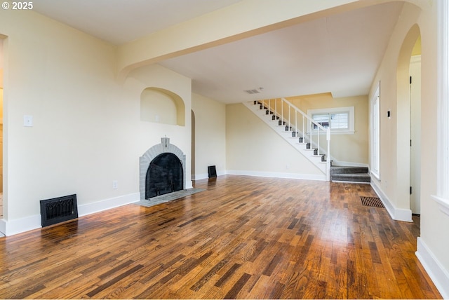 unfurnished living room featuring visible vents, baseboards, a fireplace with flush hearth, stairway, and wood finished floors