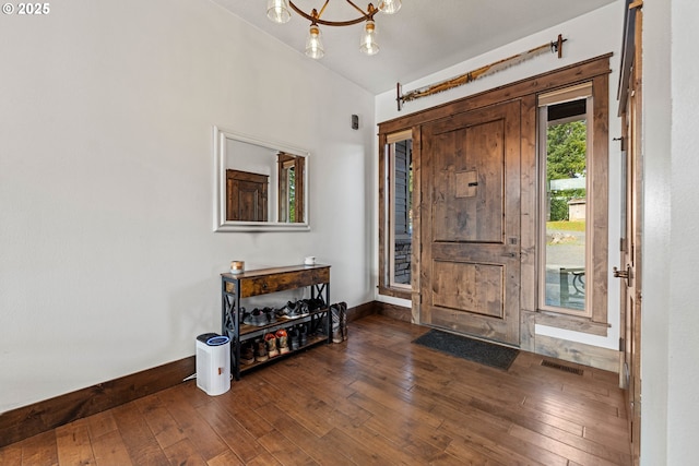 entrance foyer with a notable chandelier, lofted ceiling, wood-type flooring, visible vents, and baseboards