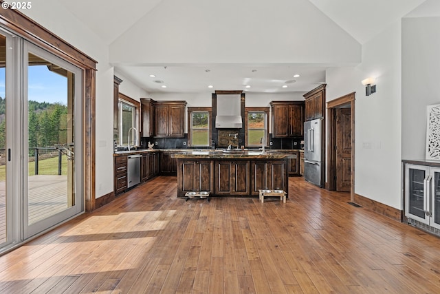 kitchen featuring hardwood / wood-style floors, wall chimney range hood, appliances with stainless steel finishes, and dark brown cabinetry