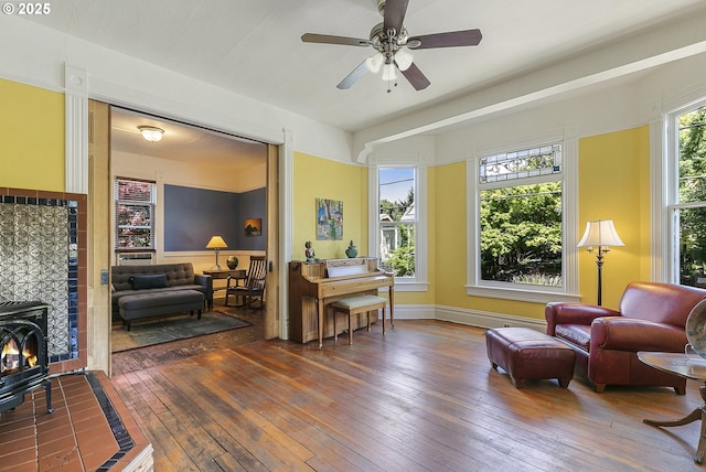 living area with wood-type flooring, ceiling fan, and a wood stove