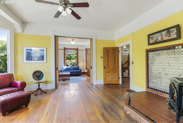 living area featuring wood-type flooring, ceiling fan, baseboards, and stairs