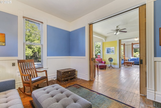 living area with a wainscoted wall, hardwood / wood-style floors, and ceiling fan