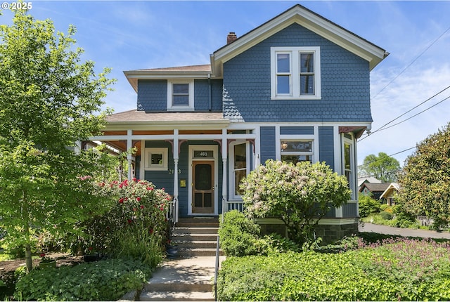 victorian house featuring a porch and a chimney