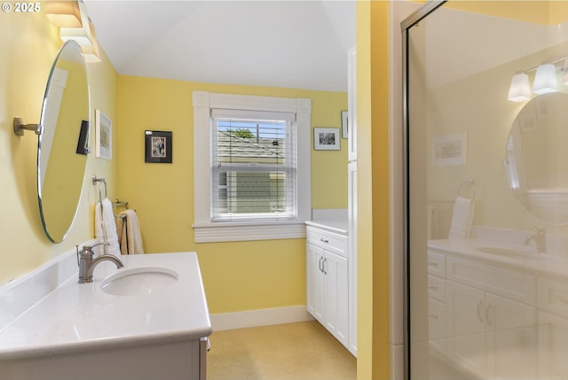 bathroom featuring baseboards, a stall shower, lofted ceiling, and two vanities