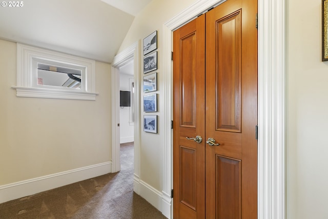 hall featuring dark colored carpet, lofted ceiling, and baseboards