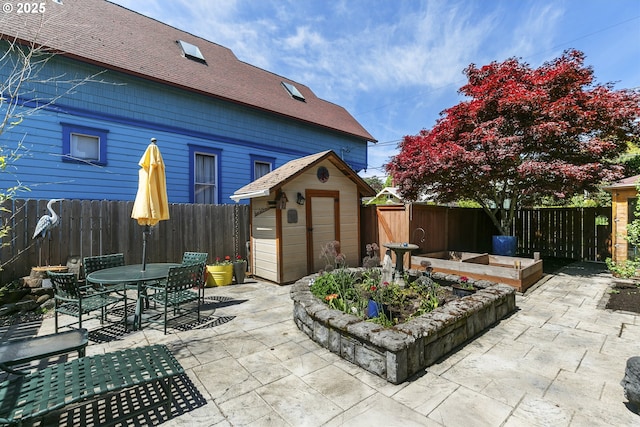 view of patio featuring outdoor dining area, an outdoor structure, a fenced backyard, and a storage unit