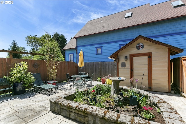 back of house featuring a patio, a shed, an outbuilding, roof with shingles, and a fenced backyard