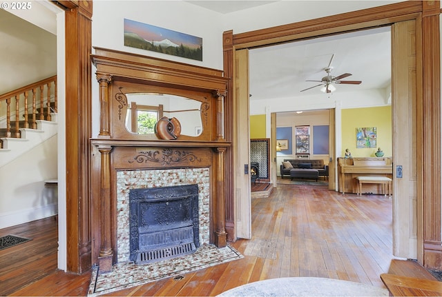 living room featuring hardwood / wood-style floors, a fireplace, ceiling fan, stairs, and baseboards