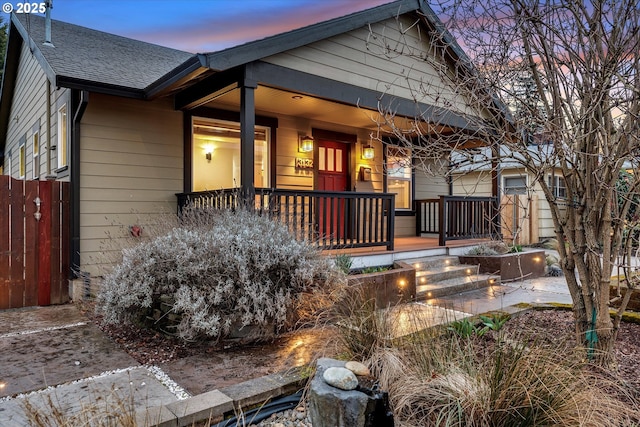 view of front of house featuring a porch, fence, and roof with shingles