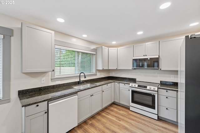 kitchen with sink, dark stone countertops, white cabinets, light hardwood / wood-style floors, and stainless steel appliances