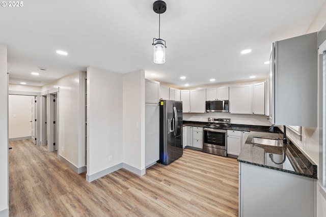 kitchen featuring pendant lighting, light hardwood / wood-style flooring, appliances with stainless steel finishes, white cabinetry, and dark stone countertops