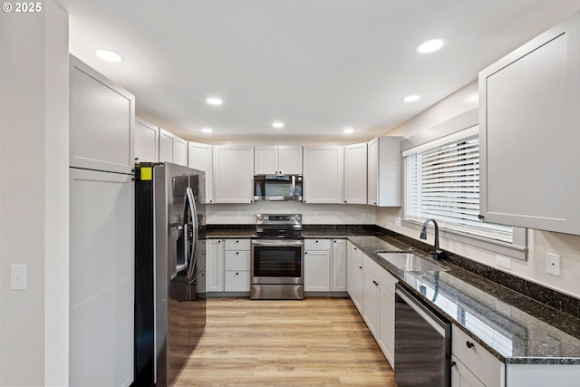 kitchen featuring appliances with stainless steel finishes, white cabinetry, sink, dark stone counters, and light hardwood / wood-style floors