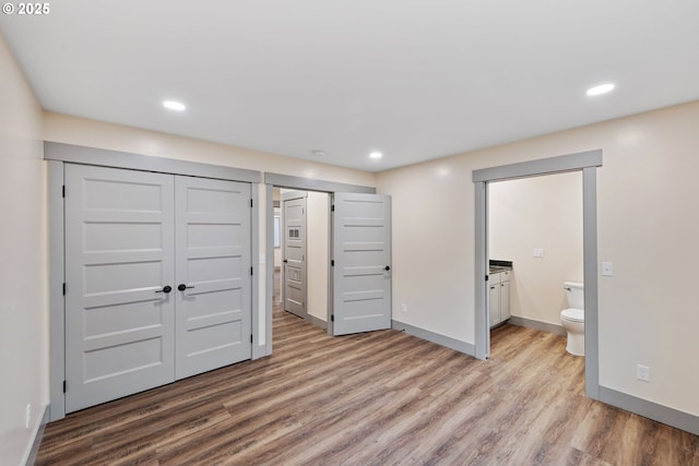 unfurnished bedroom featuring a closet, ensuite bathroom, and light hardwood / wood-style flooring