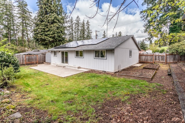 rear view of property with roof mounted solar panels, a fenced backyard, a garden, a patio area, and a lawn