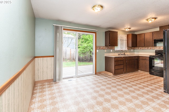 kitchen featuring baseboards, light countertops, under cabinet range hood, a sink, and black / electric stove